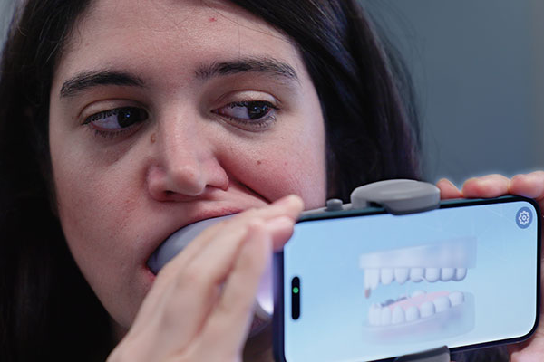 A mock patient demonstrates using a scan box and her cell phone how AI is being used in orthodontics. (Ryan Bernat/UConn Health)