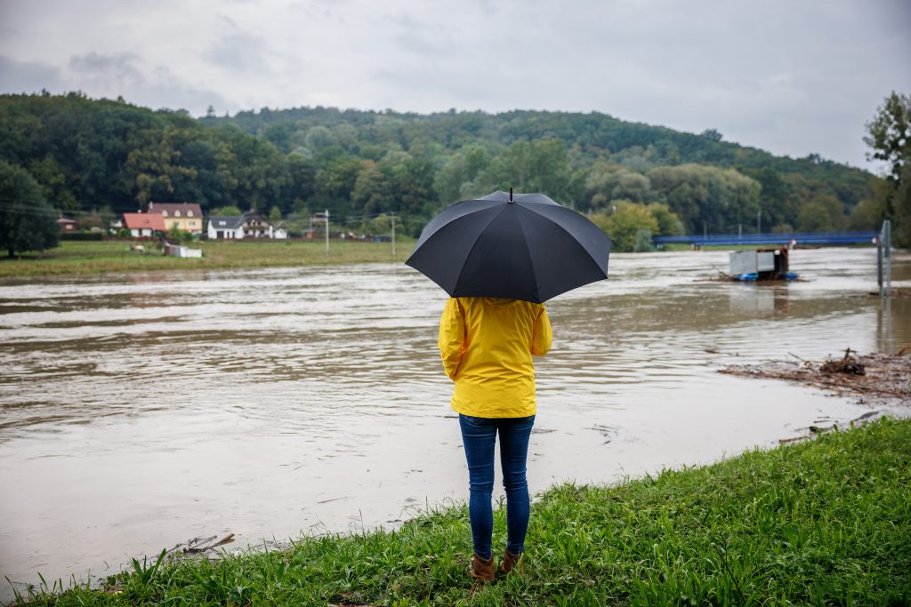 A woman holding an umbrella looks out over a flooding river.