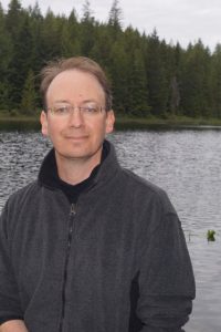 A man posing for a photo in front of a lake