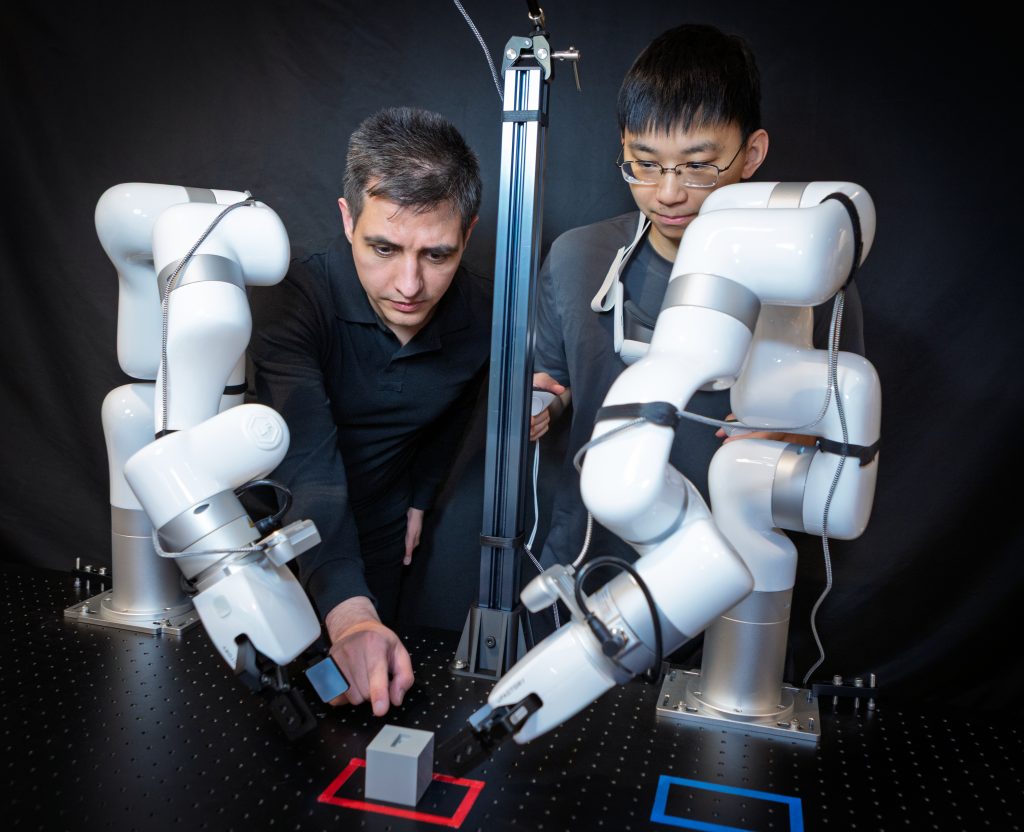 Researchers guiding robotic arms to manipulate a cube on a test platform.