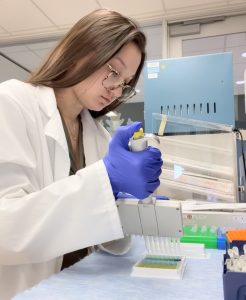 Scientist wearing a lab coat and gloves using a pipette