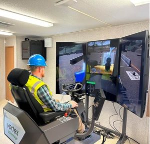A man in a hard hat using a heavy machinery simulator indoors.