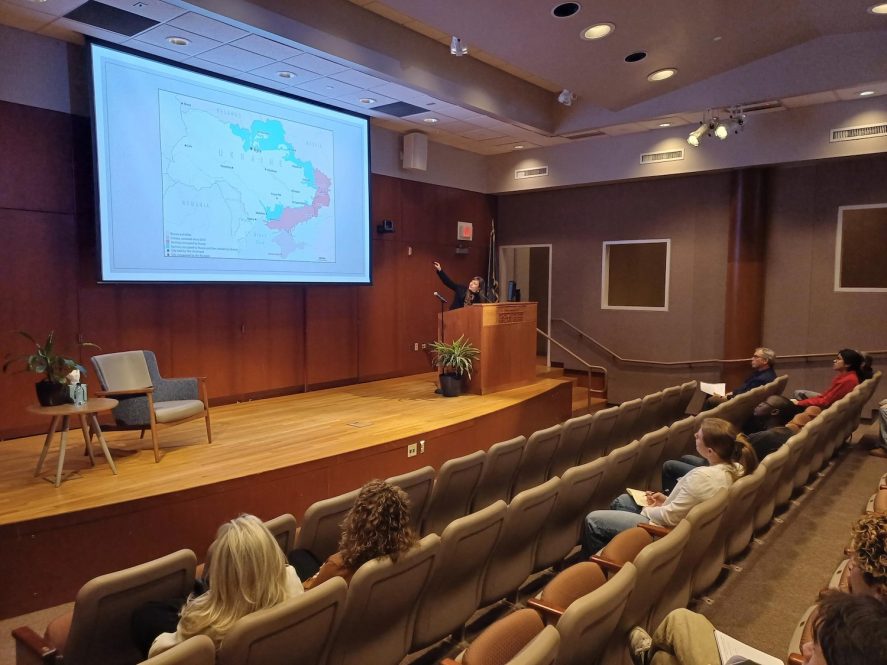 A woman pointing to a map of Ukraine and Russian-occupied regions in an auditorium