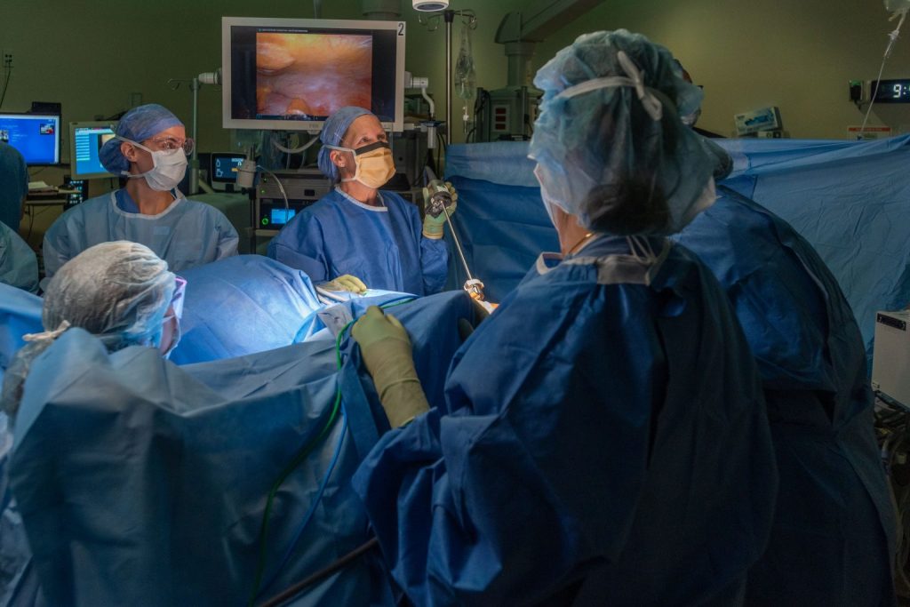 4 people wearing scrubs in an operating room performing an operation