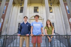 Two males and one female pose for a photo against a railing