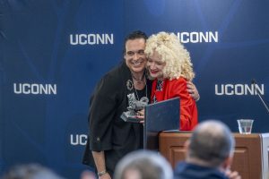 A woman in a red jacket hugging a man and presenting him an award