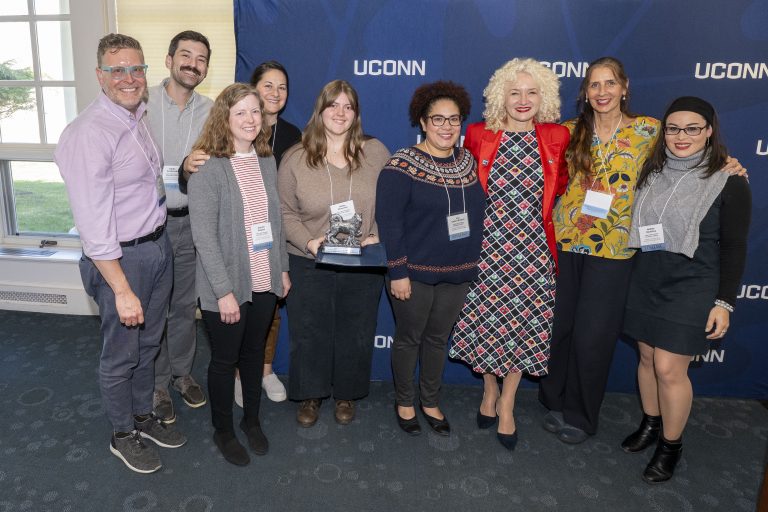 Nine people posing for a photo, holding an award