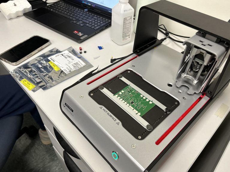 Close-up of a desktop PCB printer with a circuit board mounted on the heated platform.