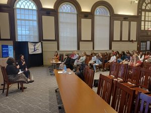 A wide shot of a large room where two speakers on the left are addressing the audience on the right.