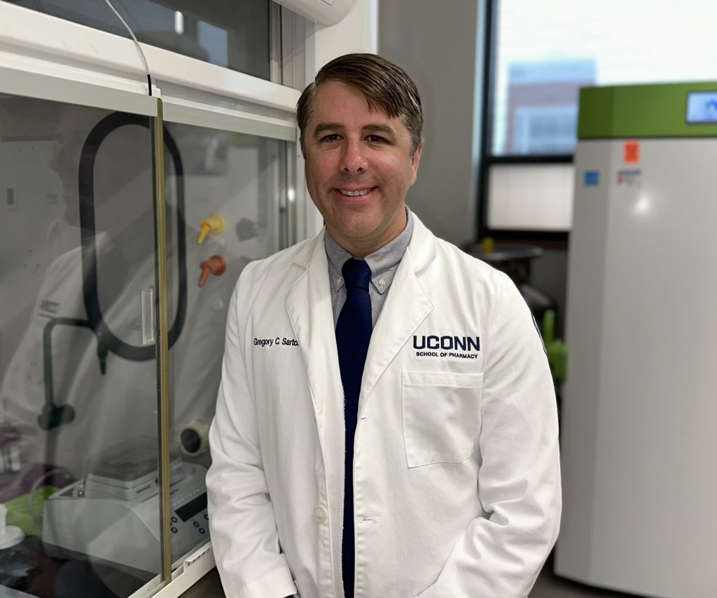 Male professor in lab coat with a dress shirt and tie stands in from of lab equipment