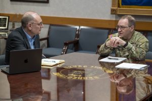 Two people sitting at a table talking with papers and laptops in front of them