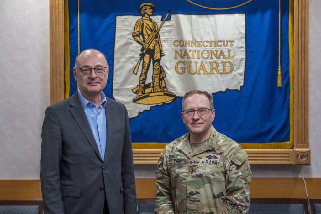 Two men standing in front of a flag that says "Connecticut National Guard"