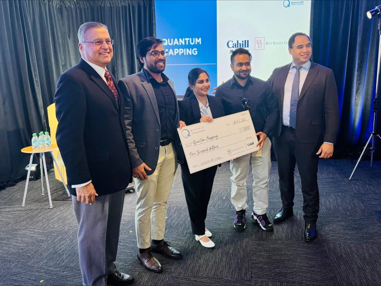 Five people pose for a group photo, with three of them holding a large novelty check.