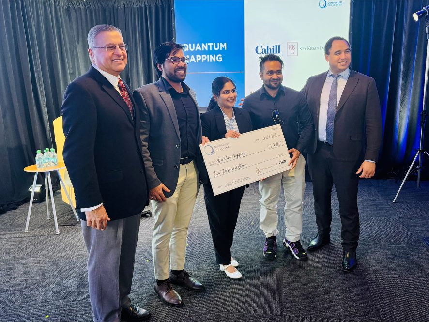 Five people pose for a group photo, with three of them holding a large novelty check.