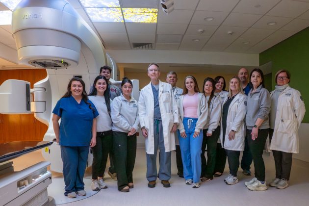 Group portrait of 13 indoors next to new radiation oncology machine