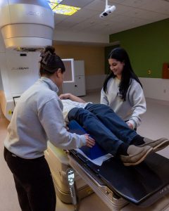 two radiation therapy technologists and a model patient demonstrate new radio-oncology equipment