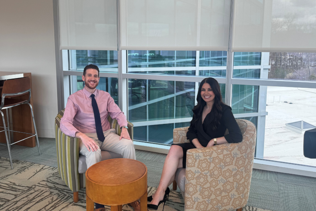 Man and woman sit in chairs smiling at camera