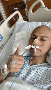 man in hospital bed with breathing equipment on giving a thumbs up