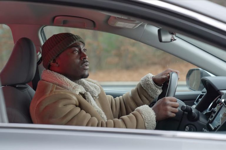 A driver grips the steering wheel while looking in the rearview mirror at flashing police lights during a traffic stop.