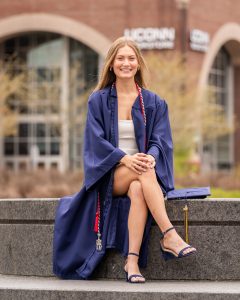 Girl poses in graduation gown on her college campus.
