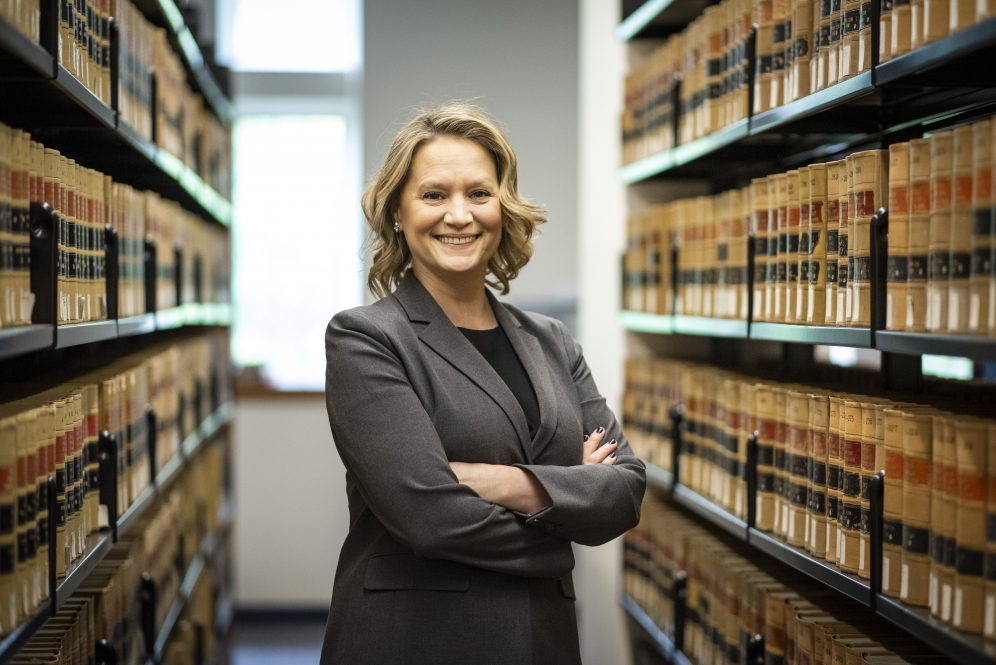 Jessica Panella stands between shelves of books with her arms crossed