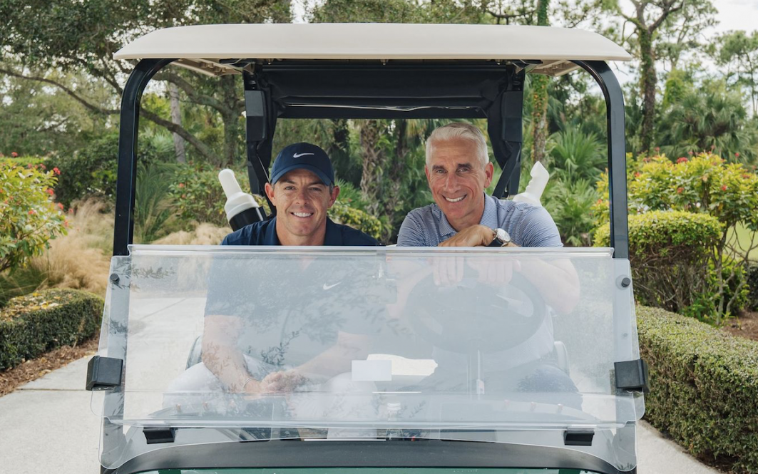 UConn alum David Abeles sits in a golf cart next to Rory McIlroy.
