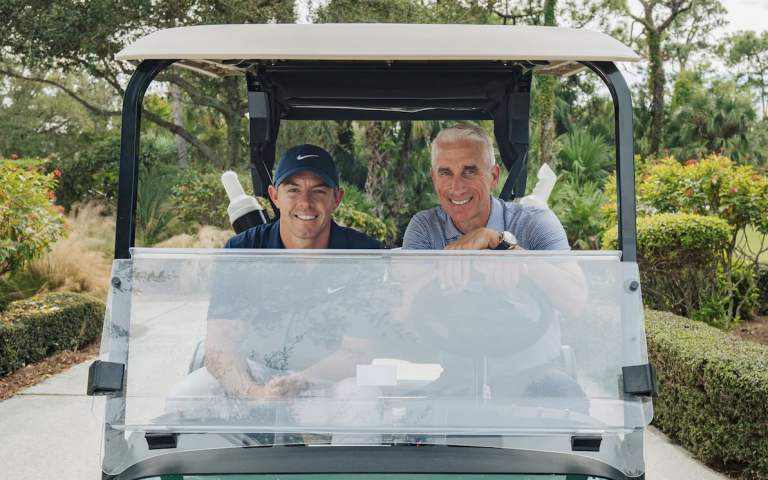 UConn alum David Abeles sits in a golf cart next to Rory McIlroy.