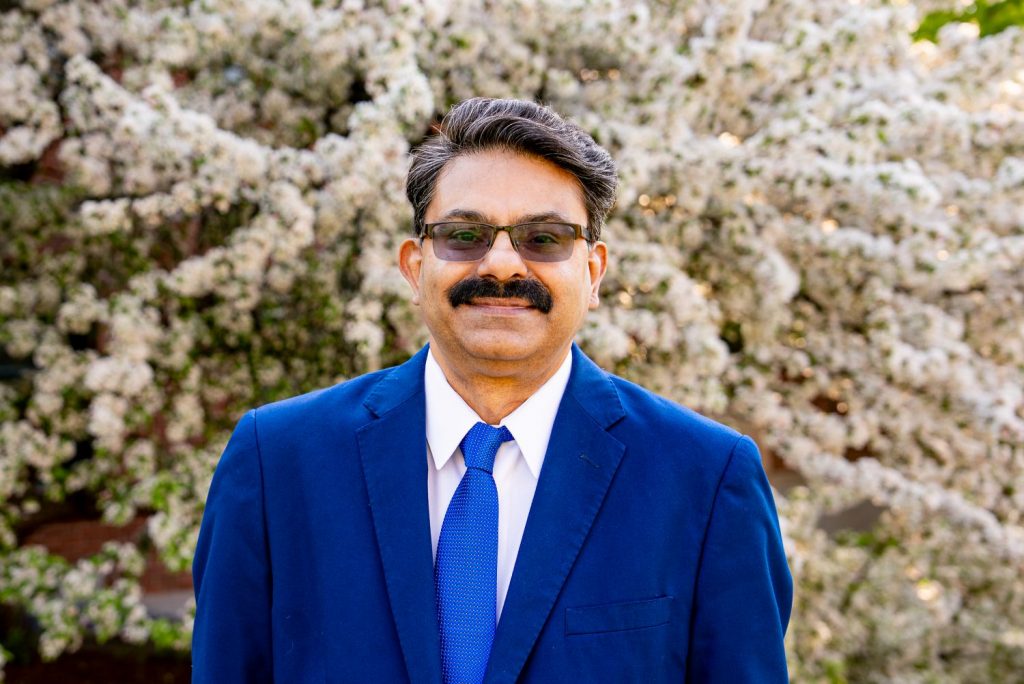 Kumar Venkitanarayanan poses in front of a flowering tree