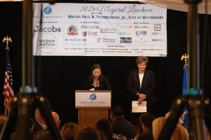 woman speaking at podium, second woman standing to left of podium