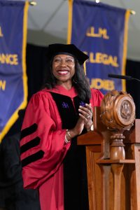 A woman in red commencement regalia smiling and clapping while standing at a podium.