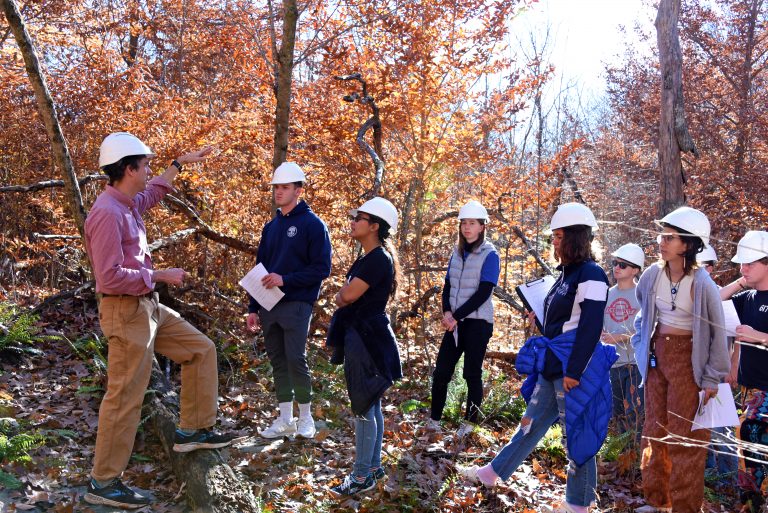 A teacher and students wearing hard hats in a forest