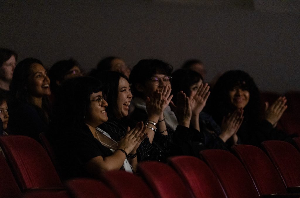 Row of people in a theatre clapping.