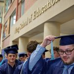 Graduates stand under the Neag School of Education sign.