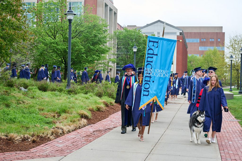 Graduates and Jonathan the Husky process outside.
