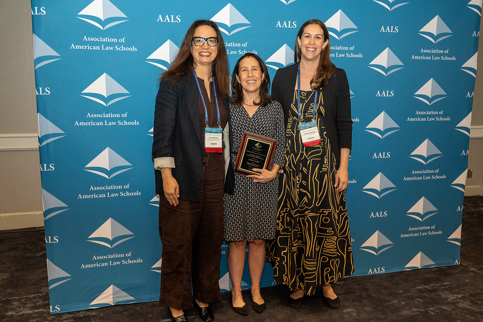 Three women standing in a line. The woman in the center is holding a plaque.
