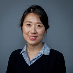 Professional headshot of a person smiling against a gray background.