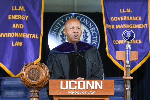 A man in graduation regalia speaking at a podium.