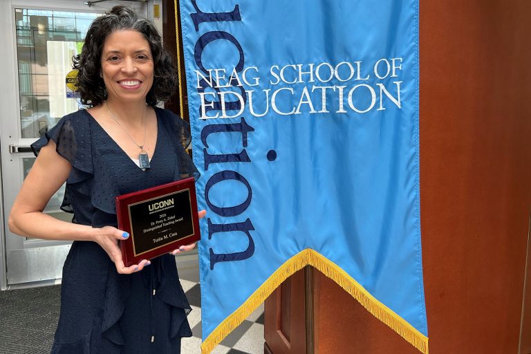 Tutita Casa stands next to the Neag School of Education banner holding her Zirkel award.