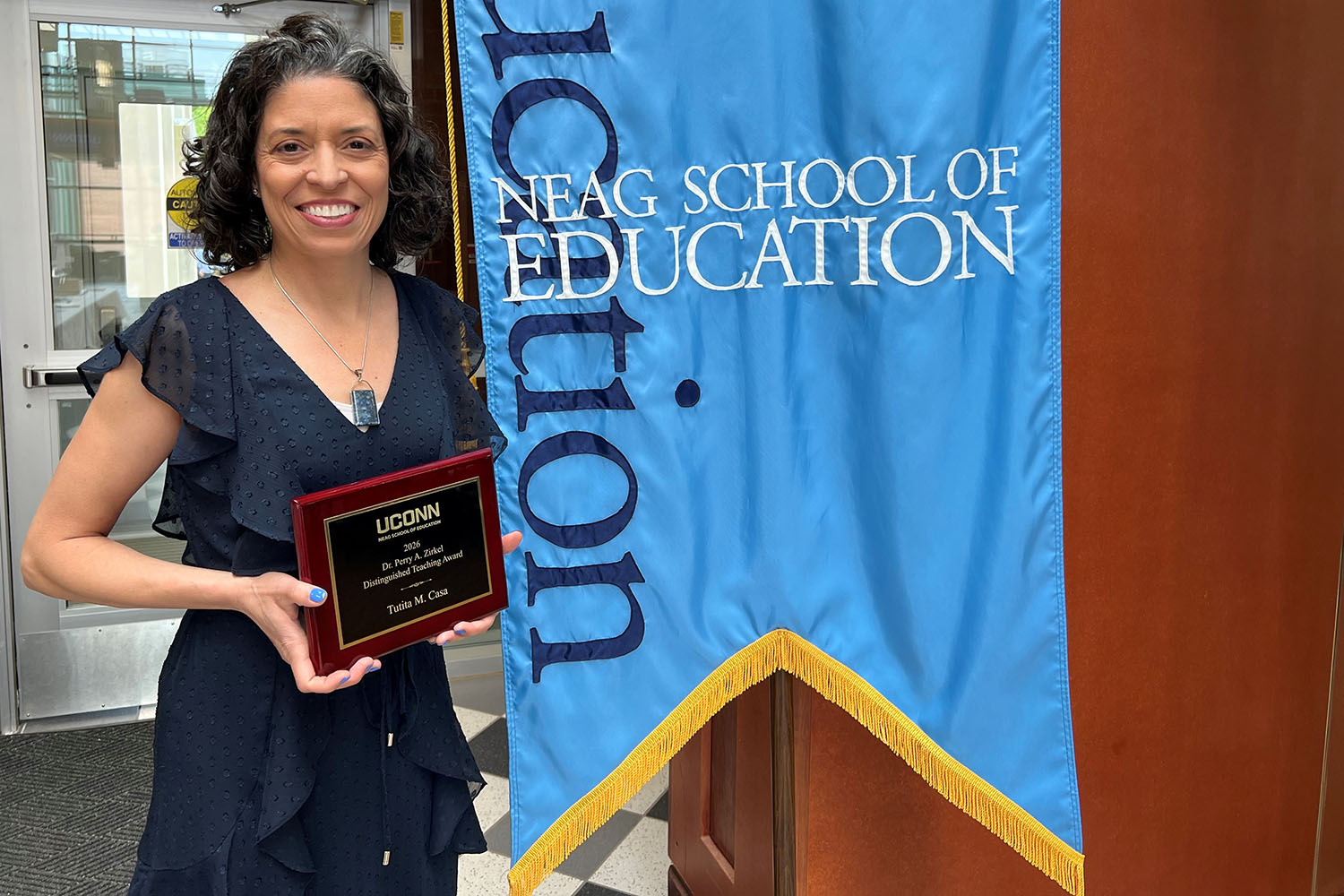 Tutita Casa stands next to the Neag School of Education banner holding her Zirkel award.