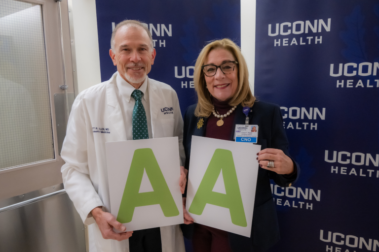 A man and woman standing in front of the uconn health logo holding signs that say 