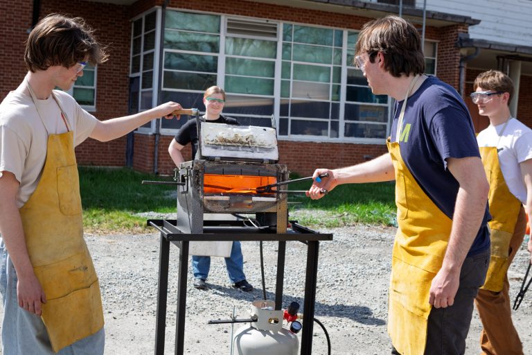 Group of students wearing safety gear and aprons work with a forge at the UConn Depot Campus.