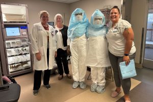 portrait of five people during personal protective equipment training, with two in PPE