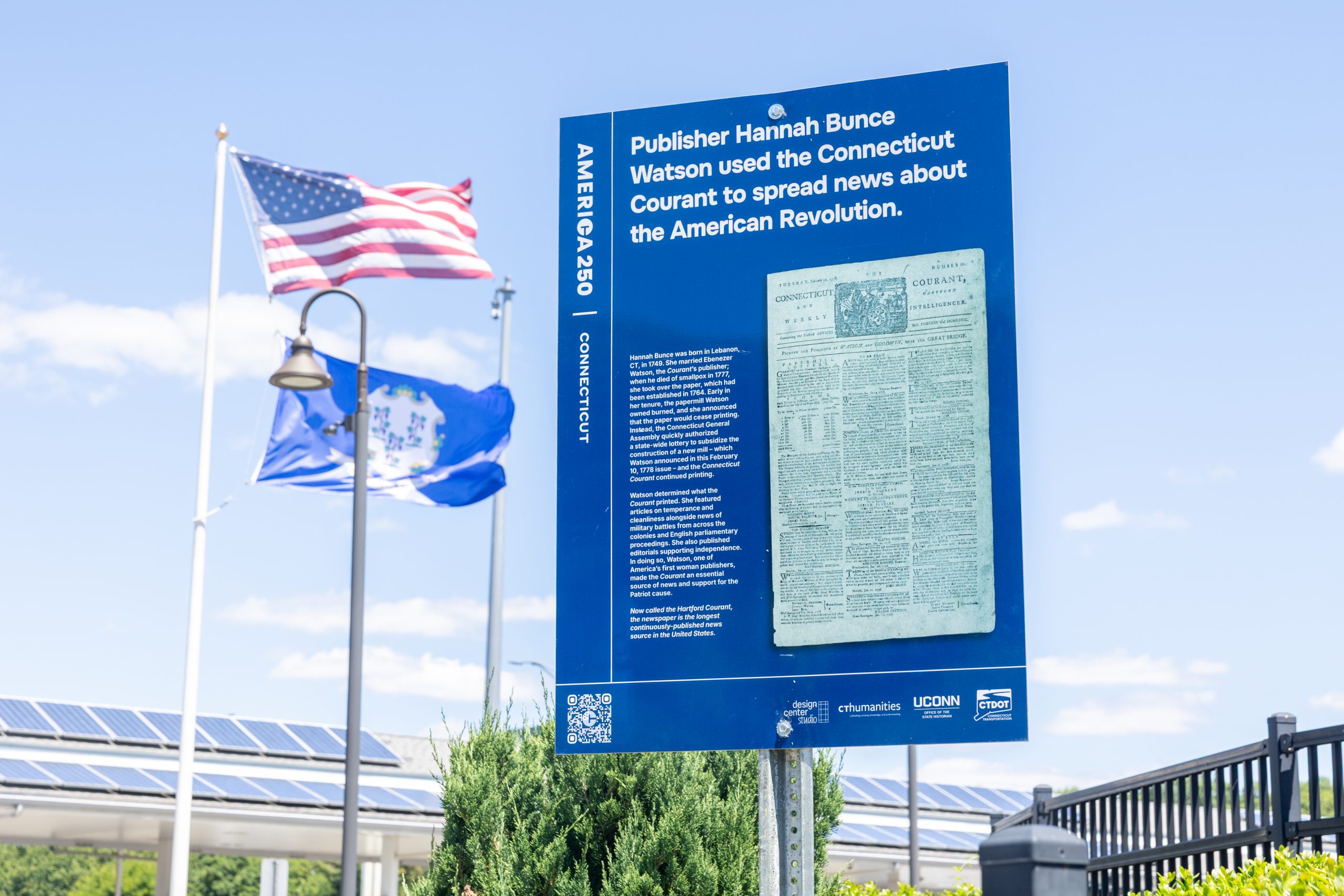 A Connecticut America 250 sign with information about the Hartford Courant with a Connecticut flag and U.S.A flag next to it