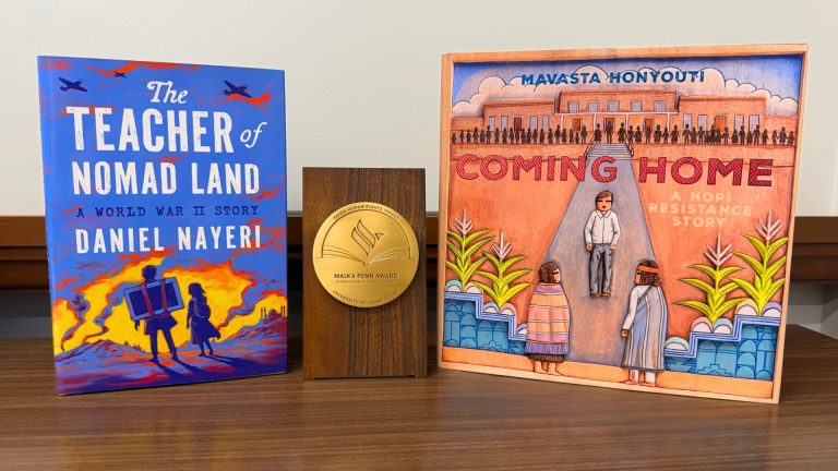The award winning books of the Malka Penn Award for Human Rights in Children's Literature, arranged standing aside a golden medal.