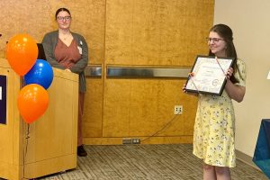 Woman holds certificate, second woman looks on