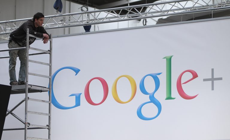 A man stands on a scaffold in front of a huge screen that reads 
