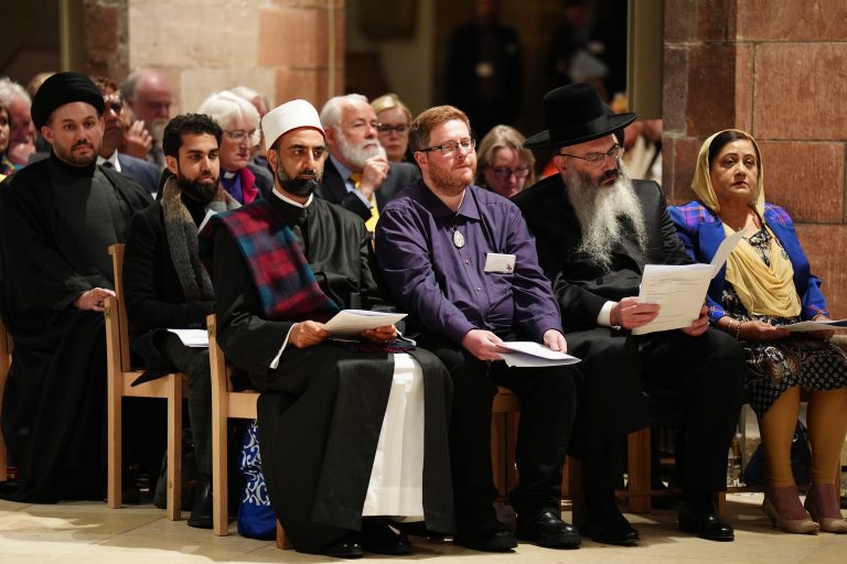 People wearing the traditional garments of members of different religious faiths sit together during an interfaith prayer service.