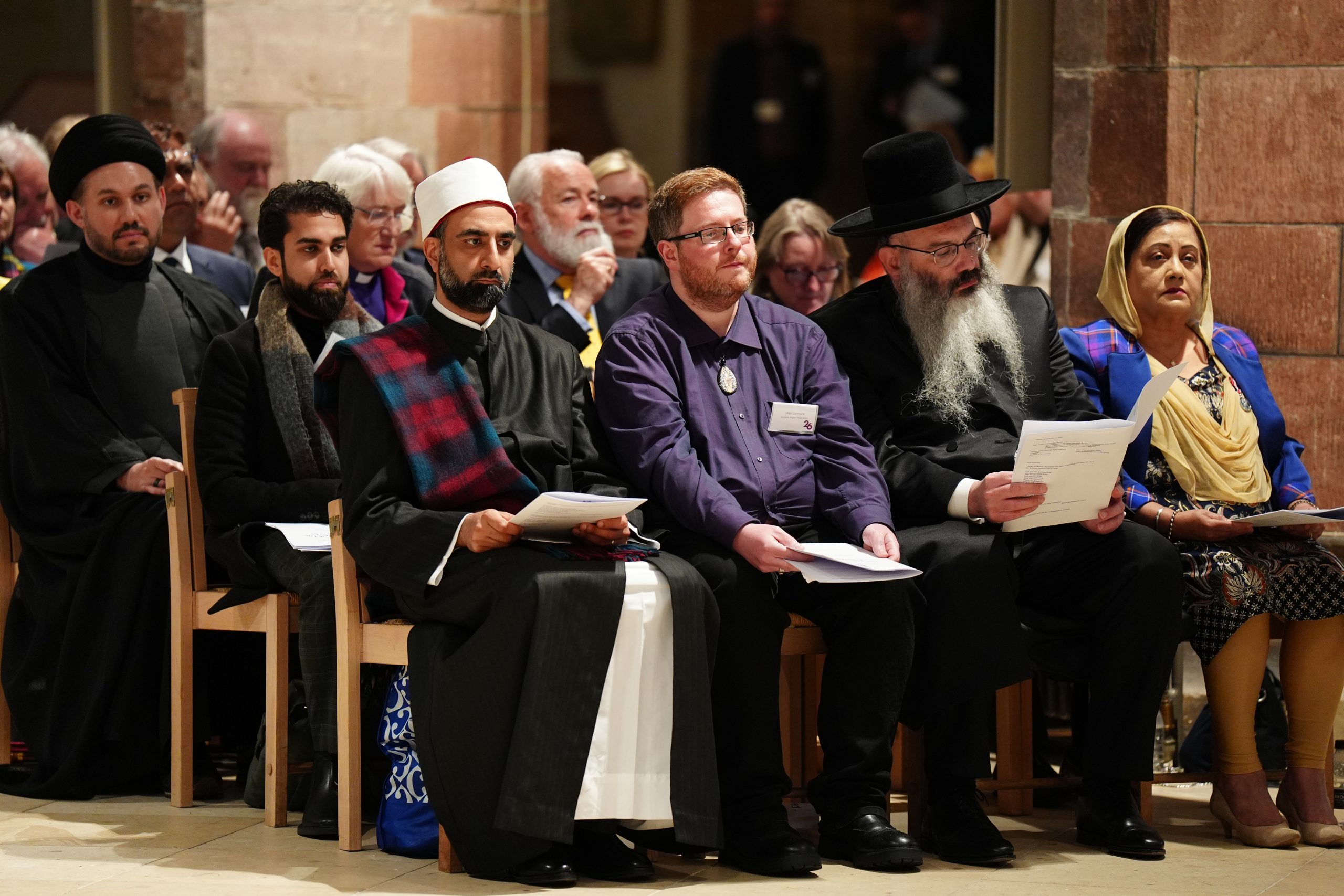 People wearing the traditional garments of members of different religious faiths sit together during an interfaith prayer service.