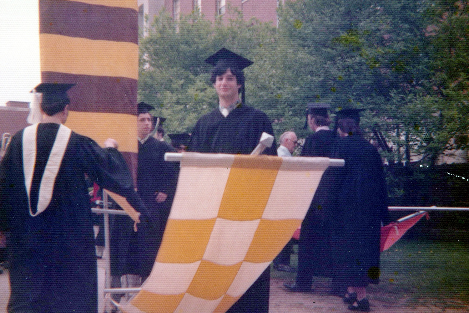 A male in graduation regalia holding a graduation banner