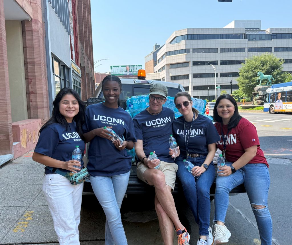 Five people standing by a vehicle with cases of water